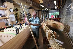 Boat builder fitting a long wooden hull in his shop