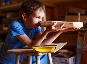 Boy sighting along the hull of a small model boat