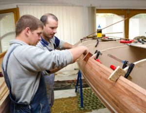Two men clamping the planks of a wooden boat