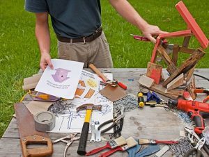 Birdhouse instructions, hand tools and a half-built project on an outdoor work table