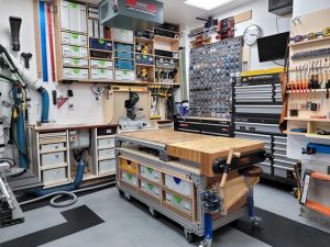 Organized workshop with a mobile workbench, wall cabinets and a wall of storage bins
