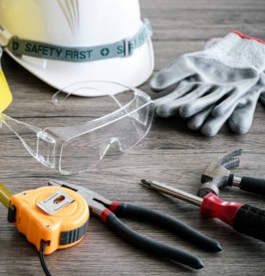 Safety gear on a workbench: hard hat, glasses, gloves, tape measure and pliers