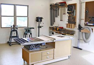 Small shop with a table saw cabinet, a drill press, a band saw and wall-mounted clamps