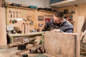 Woodworker using a chisel on a board in a wood-paneled shop